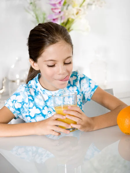 Pequena menina língua para fora olhando suco de laranja — Fotografia de Stock