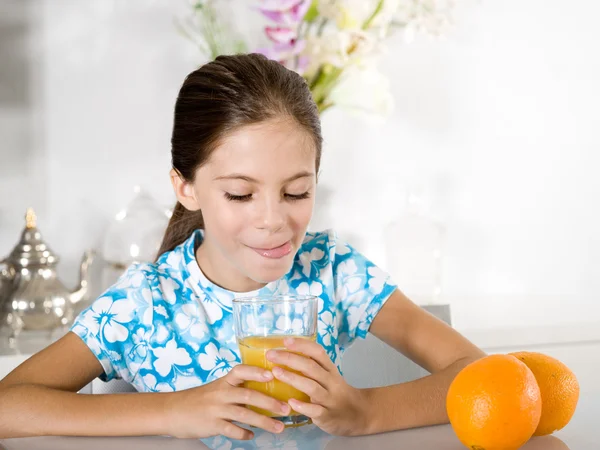 Pequena menina língua para fora olhando suco de laranja — Fotografia de Stock