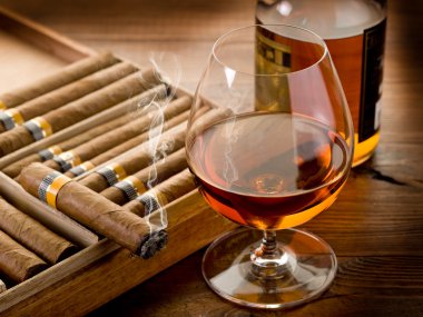 Cuban cigar and bottle of cognac on wood background clipart