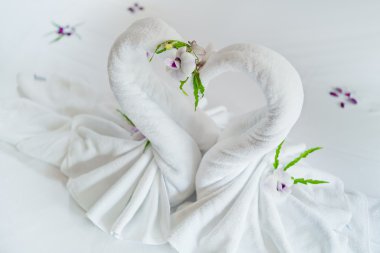 Close up view of two nice towels swans on white bed sheet clipart