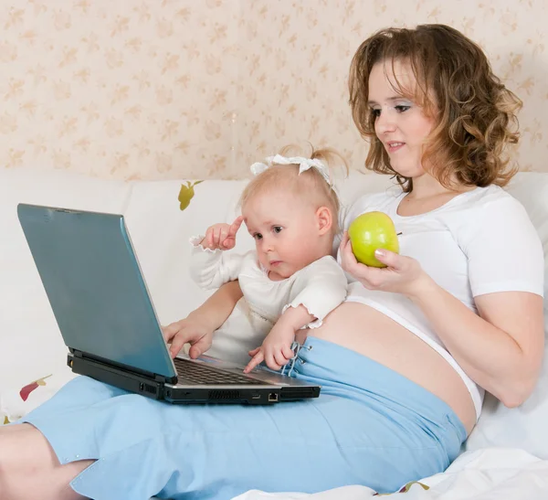 Gravid kvinna med dotter och den bärbara datorn — Stockfoto