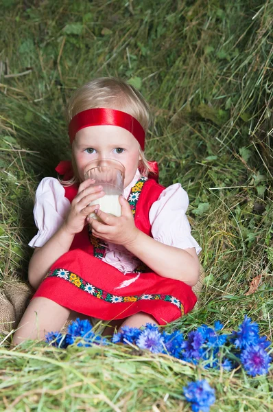 La niña con un vaso de leche en el heno — Foto de Stock