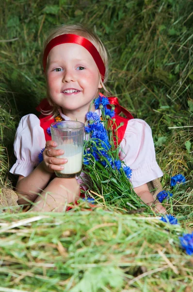 Malá holčička se sklenkou mléka na seno — Stock fotografie