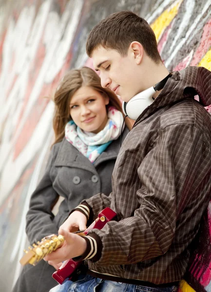 Tiener paar met gitaar bij graffiti achtergrond. — Stockfoto