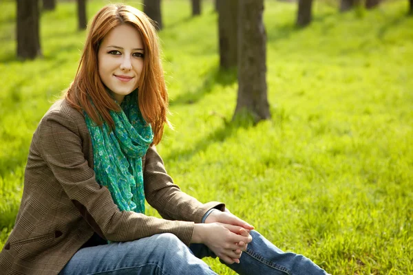 Hermosa chica pelirroja sentada en la hierba verde en el parque . — Foto de Stock