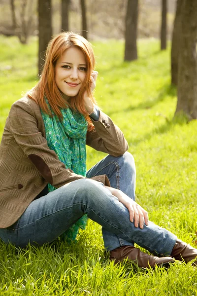 공원에서 푸른 잔디에 앉아 아름 다운 빨간 머리 소녀. — 스톡 사진