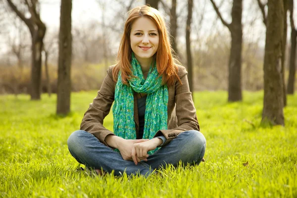 Beautiful red-haired girl sitting at green grass at park. — Stock Photo, Image