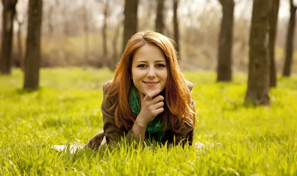 Menina ruiva bonita sentada na grama verde no parque . — Fotografia de Stock