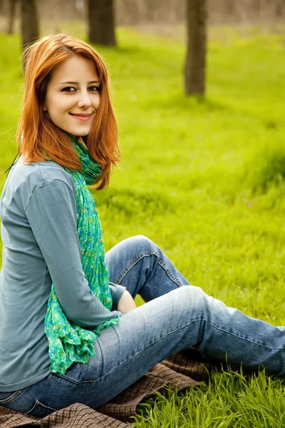 漂亮的红发女孩坐在绿草在公园. — 图库照片