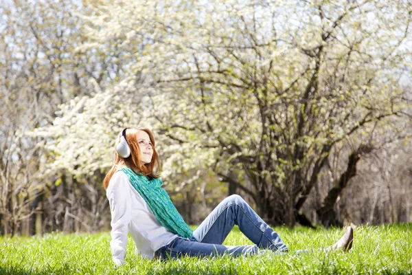 Rödhårig tjej med hörlurar i parken. — Stockfoto