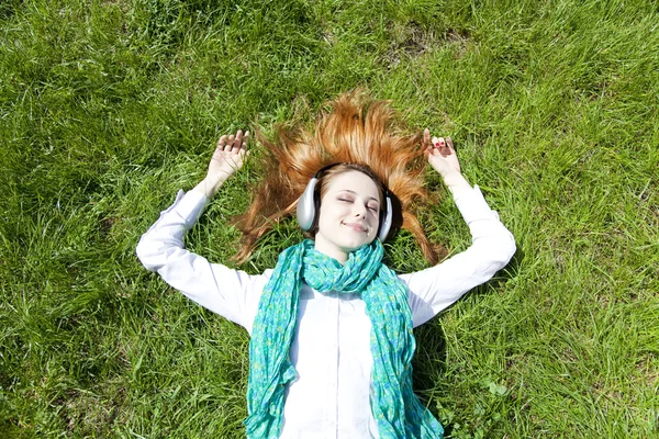 Руда дівчина з навушниками лежить в парку . — стокове фото