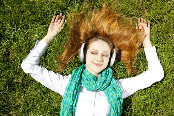 Redhead girl with headphone lies in the park. — Stock Photo, Image