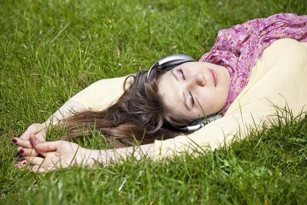 Brunette girl with headphone lies in the park. — Stock Photo, Image