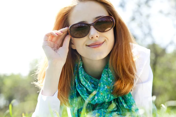 Belle fille aux cheveux roux en lunettes de soleil au parc . — Photo