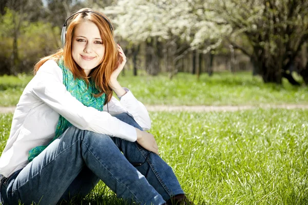 Rusovláska dívka s sluchátka v parku. — Stock fotografie