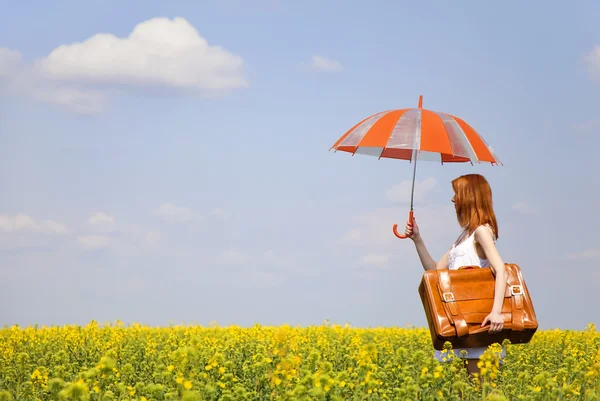 Rödhårig enchantress med paraply och resväska på våren rapesee — Stockfoto