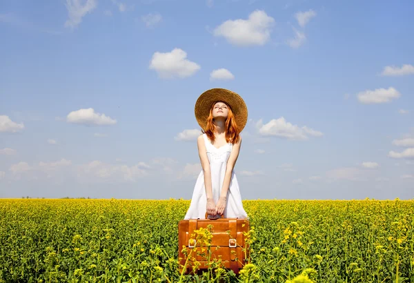春の菜種のフィールドでスーツケースと赤毛の魔性の女. — ストック写真