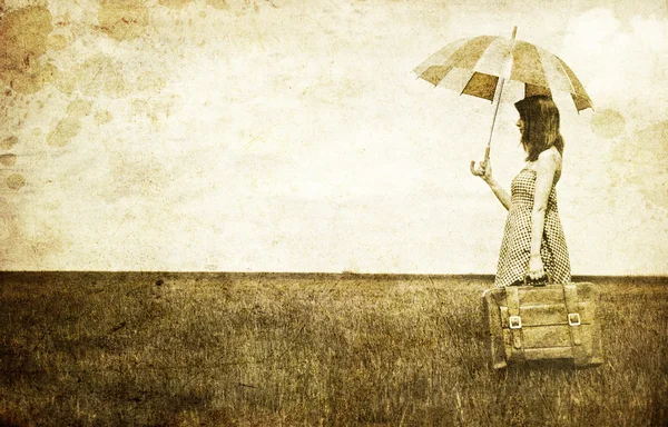 Рыжая волшебница с зонтиком и чемоданом на весенней пшенице — стоковое фото