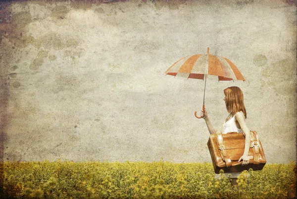 Rothaarige Zauberin mit Regenschirm und Koffer am Frühlingsrapsee — Stockfoto