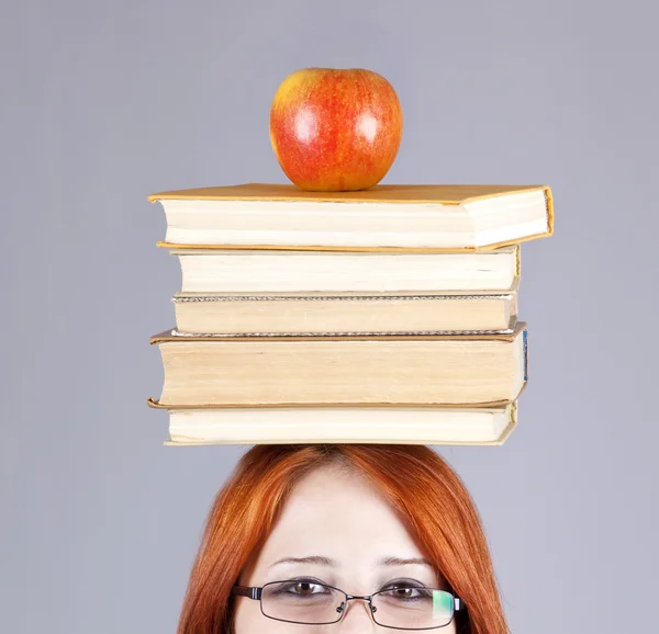 Rödhårig flicka hålla apple och böcker på huvudet. — Stockfoto