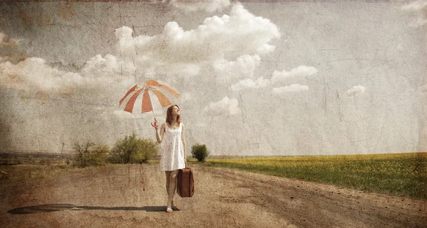Eenzaam meisje met koffer en paraplu bij landweg. — Stockfoto