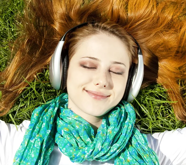 Redhead girl with headphone lies in the park. — Stock Photo, Image