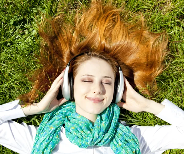 Rödhårig flicka med hörlurar ligger i parken. — Stockfoto