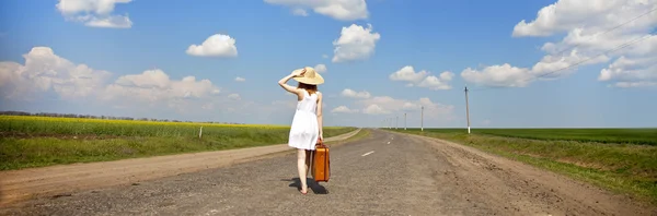 Einsames Mädchen mit Koffer an der Landstraße. Panoramafoto. — Stockfoto