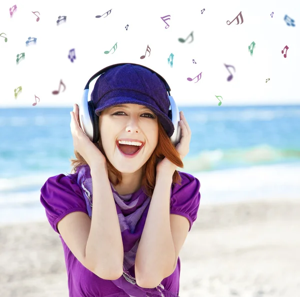 Flicka med hörlurar och anteckningar på stranden. — Stockfoto