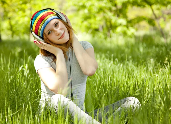 Руда дівчина з навушниками на зеленій траві . — стокове фото