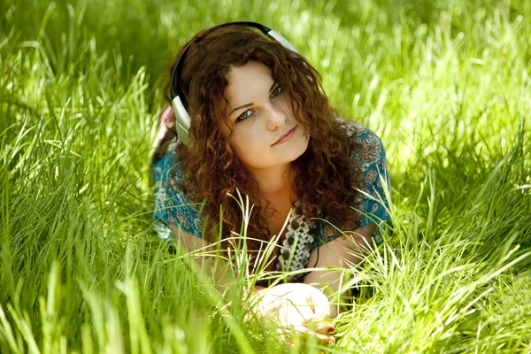 Roodharige meisje met hoofdtelefoon op groen gras. — Stockfoto