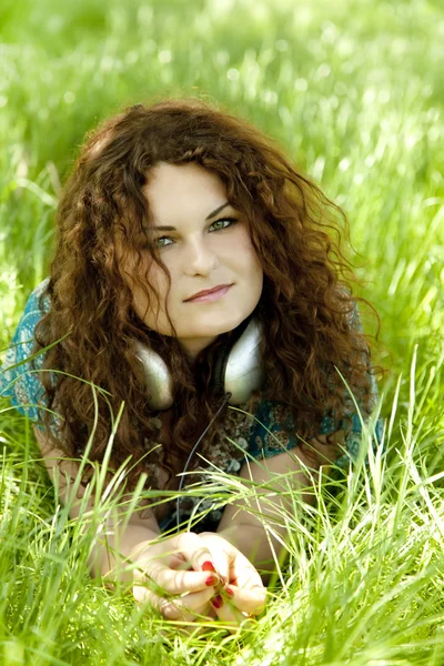 Roodharige meisje met hoofdtelefoon op groen gras. — Stockfoto