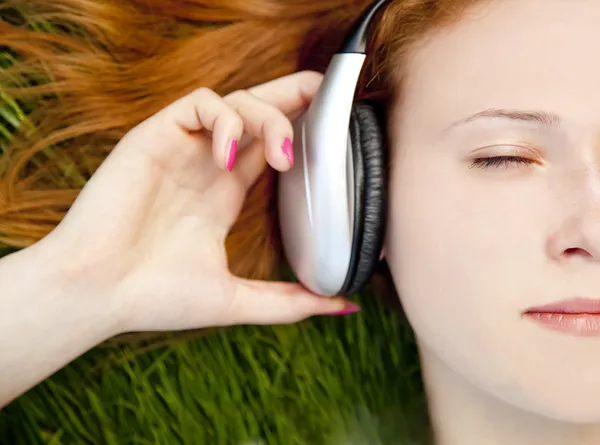 Рыжая девушка слушает музыку на зеленой траве . — стоковое фото