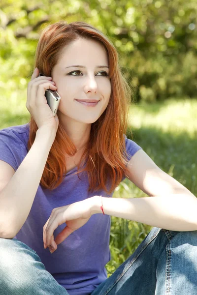 Mooi roodharig meisje met mobiele telefoon in het park in zomer t — Stockfoto