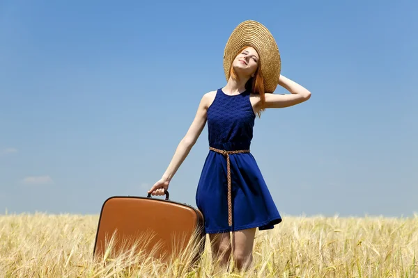 Rusovláska dívka s kufrem na jaře pšeničné pole. — Stock fotografie