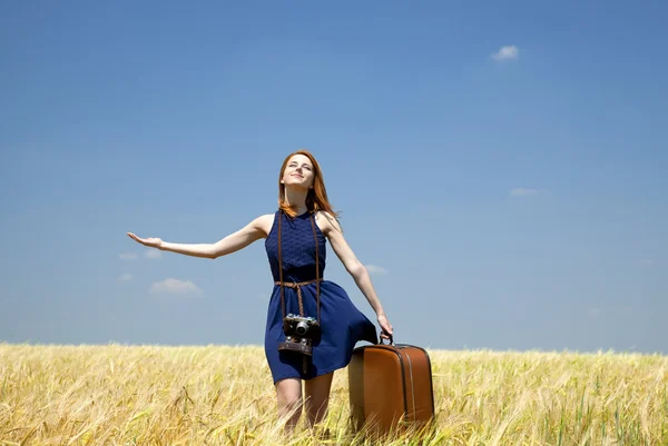 Redhead girl with suitcase at spring wheat field. — Stock Photo, Image