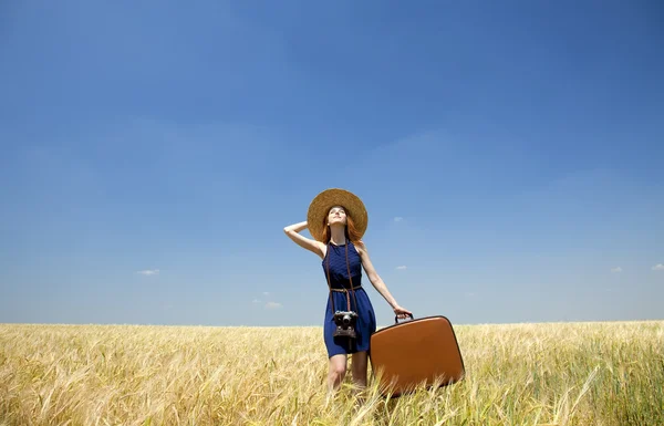 Ragazza rossa con valigia al campo di grano primaverile . — Foto Stock