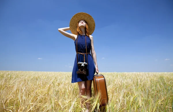 Vöröshajú lány a tavaszi búza field bőrönddel. — Stock Fotó
