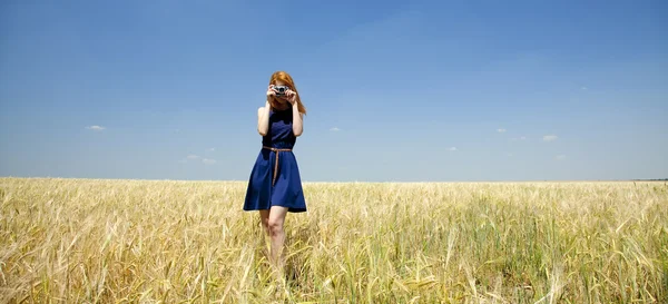 Ruda dziewczyna w wiosna pole z retro aparat. — Zdjęcie stockowe