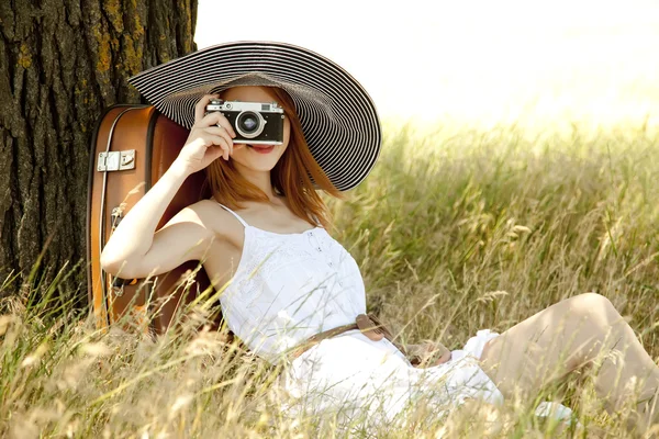 Rödhårig flicka sitter nära träd med vintage kamera. — Stockfoto