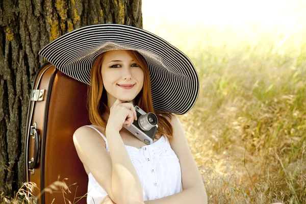 Rödhårig flicka sitter nära träd med vintage kamera. — Stockfoto