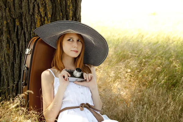 Rusovláska dívka sedí u stromu s vinobraní fotoaparát. — Stock fotografie