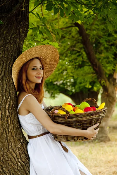 Mooi roodharig meisje met vruchten in mand op tuin. — Stockfoto