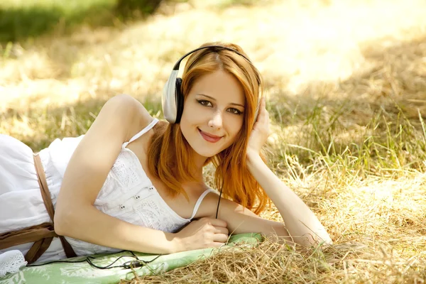 Belle rousse fille avec écouteurs au jardin . — Photo