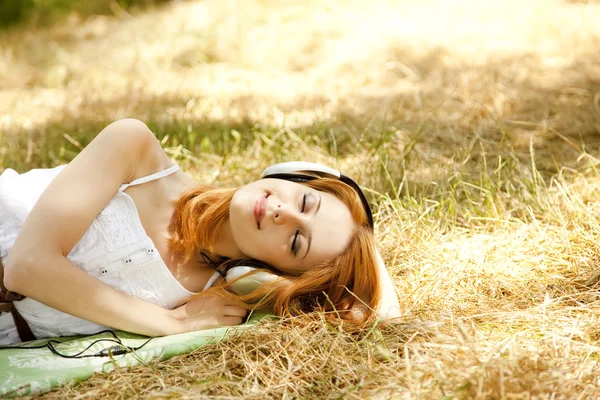 Mooi roodharig meisje met koptelefoon op tuin. — Stockfoto