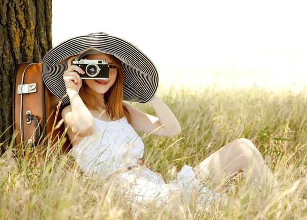 红发女孩坐在树旁用老式相机. 图库图片