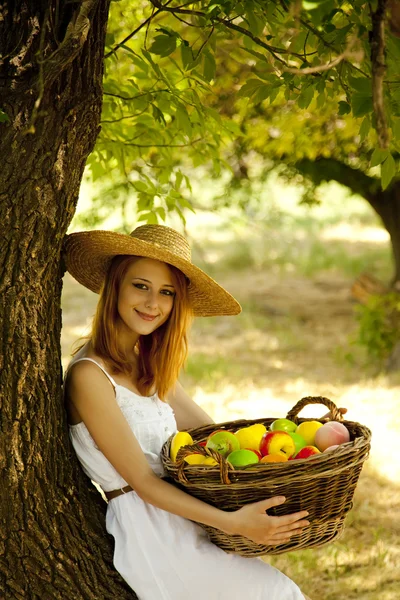 Beautiful redhead girl with fruits in basket at garden. Stock Photo
