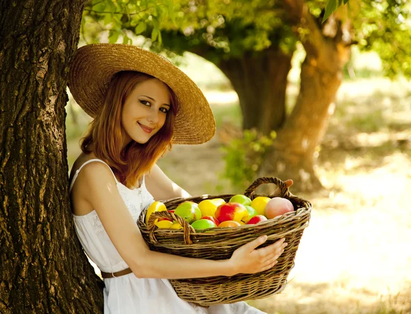 Beautiful redhead girl with fruits in basket at garden. Stock Picture
