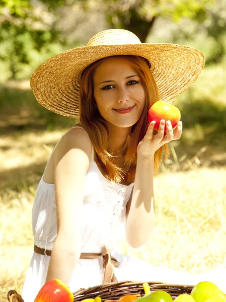Όμορφη κοκκινομάλλα κοπέλα με τα φρούτα στο καλάθι σε κήπο. — Φωτογραφία Αρχείου