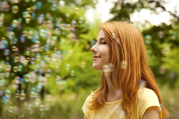 Redhead girl in the park under soap bubble rain. — Stock Photo, Image